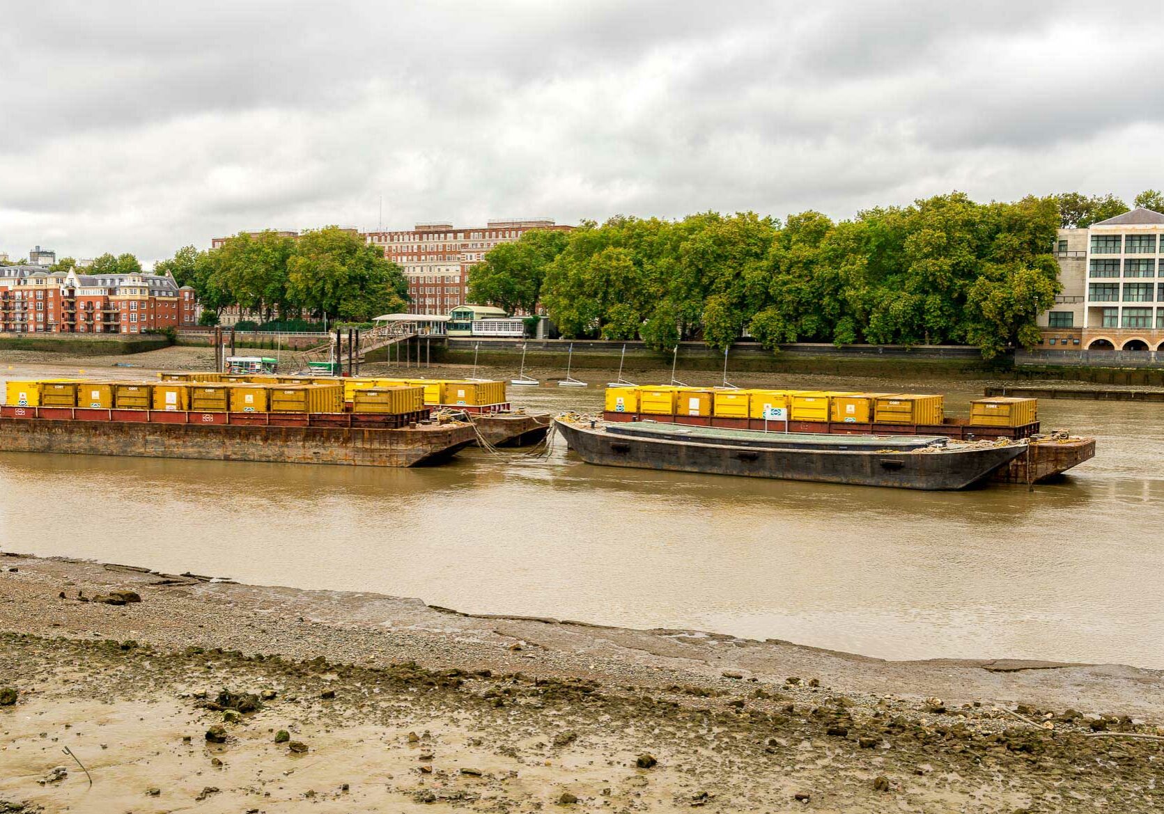Dirty shores of the river Thames in London, and barges loaded with containers