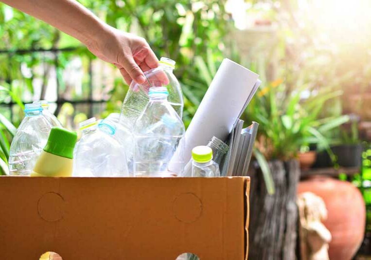 A hand placing an empty plastic bottle in a recycling box